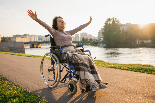 Woman using a wheelchair outdoors with her arms raised